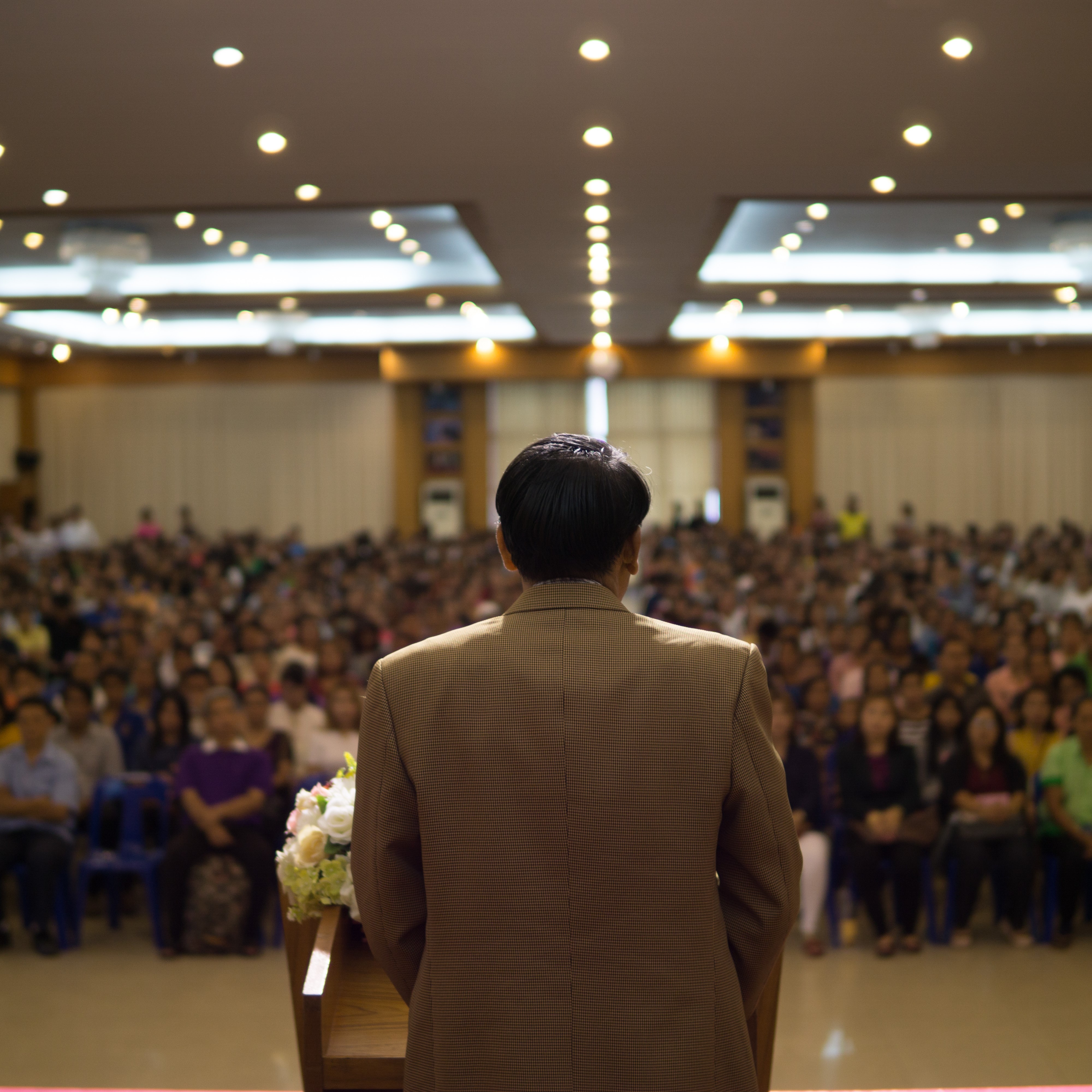 Stock image of back of man at podium speaking to an audience