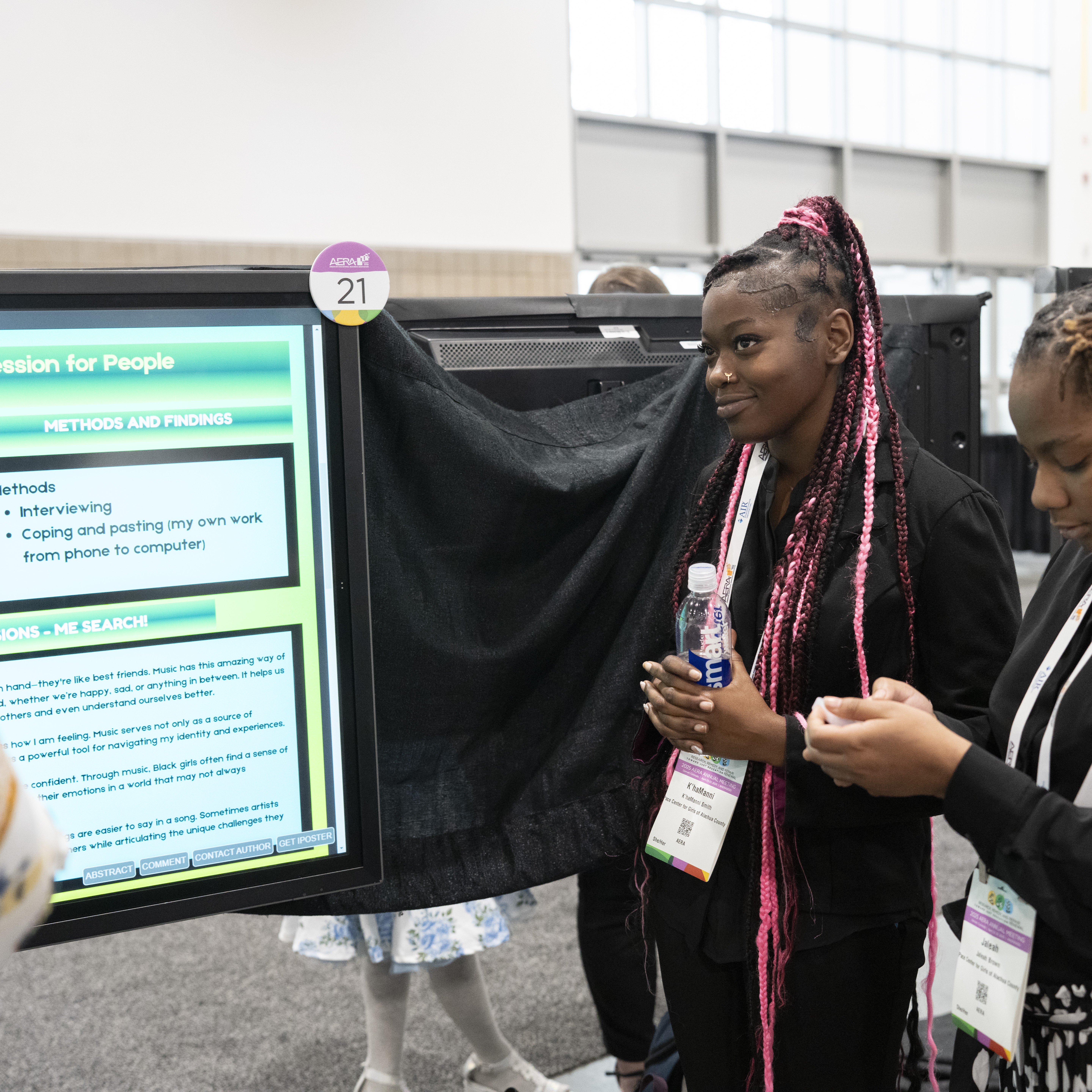 A high school age girl stands next to a poster and looks down at it