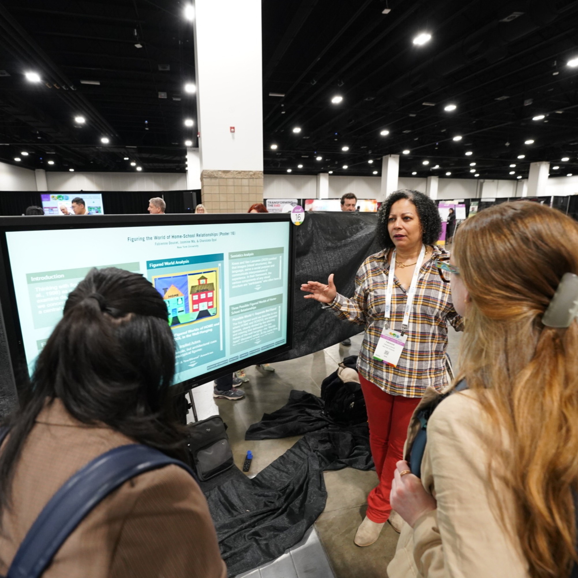 A person stands next to a poster speaking to a group who are standing with their backs to the camera