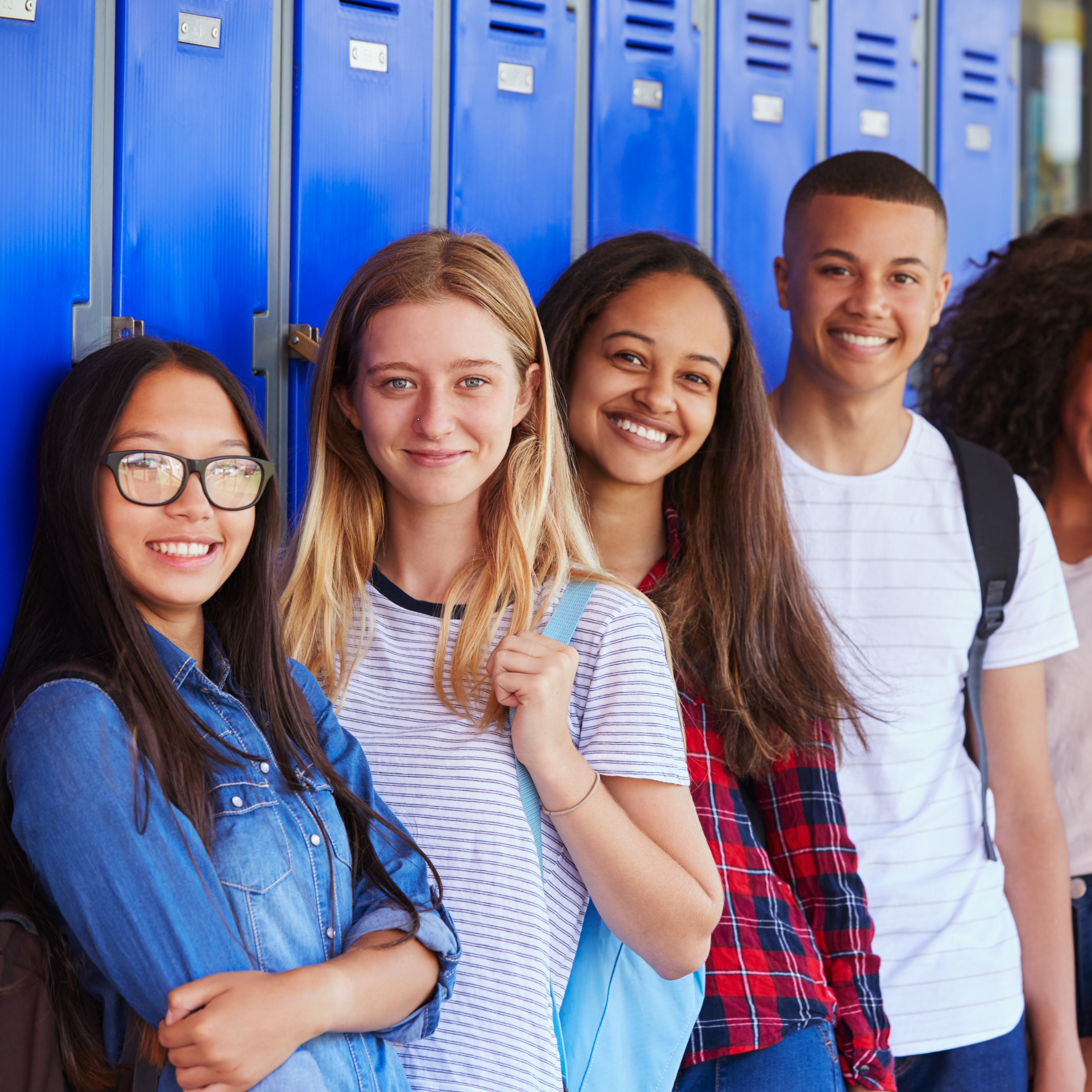 Diverse group of middle school aged kids next to locker smiling at camera