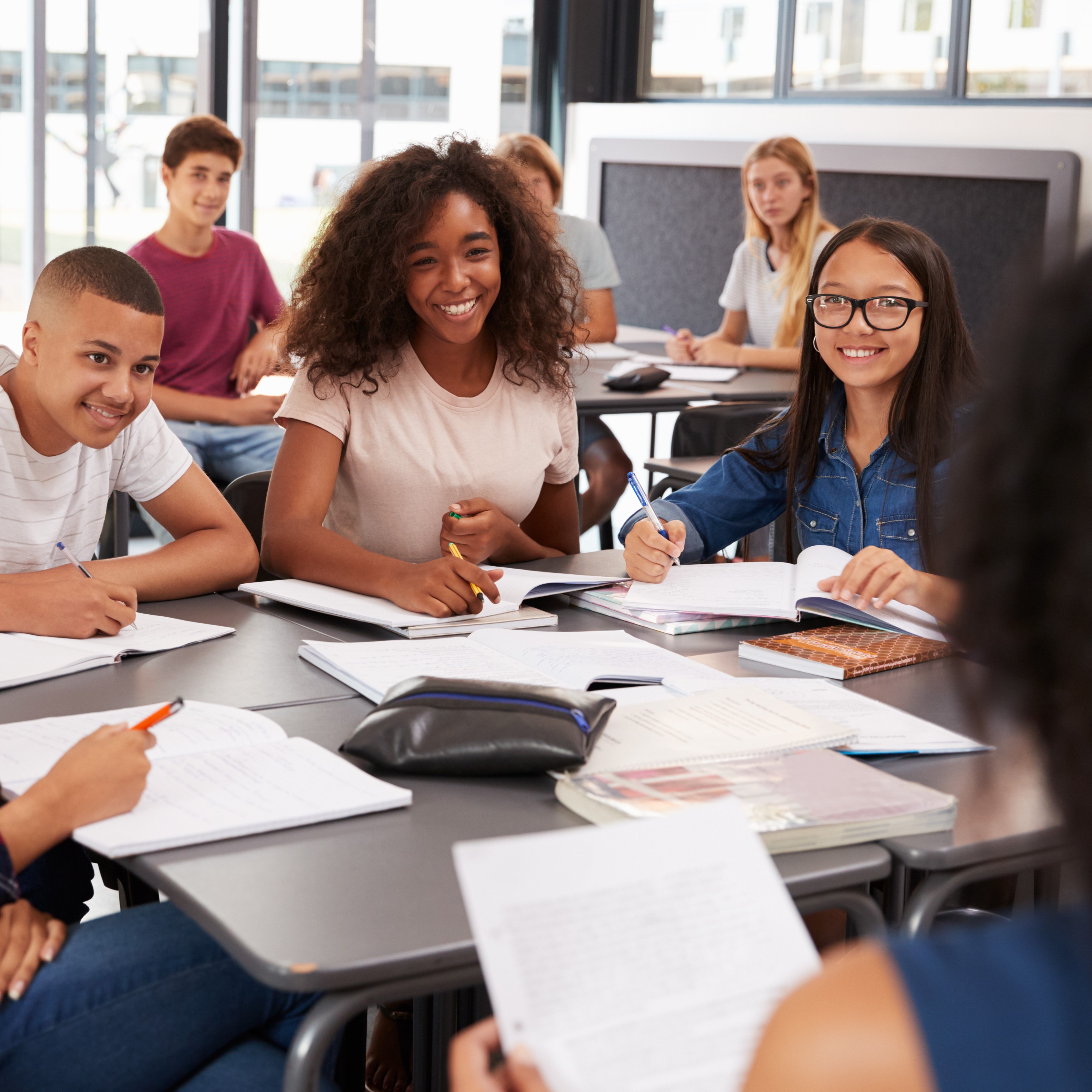 Diverse group of middle school aged kids next to locker smiling at camera